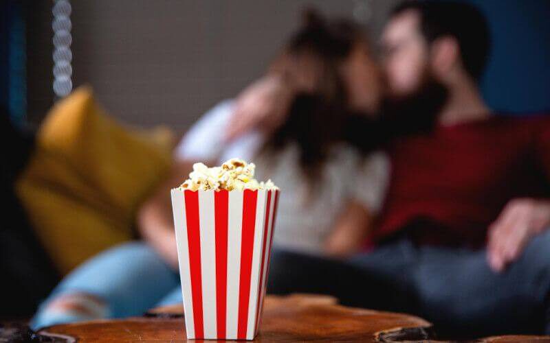 film na romantyczny wieczór oglądane przez całującą się parę z popcornem na pierwszym planie